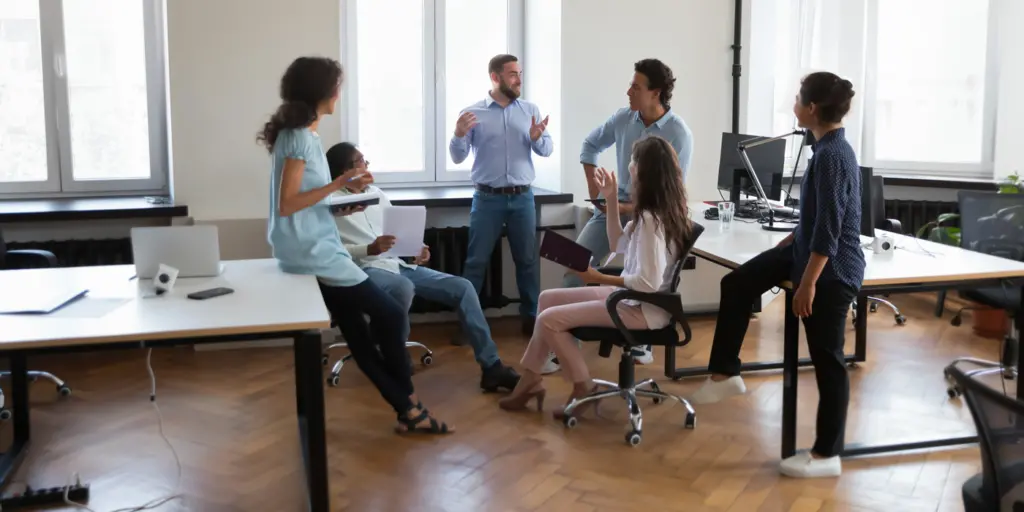 Quattro professionisti sorridenti riuniti attorno a un tavolo modulare in una luminosa sala riunioni a Torino all'interno del nostro Coworking.