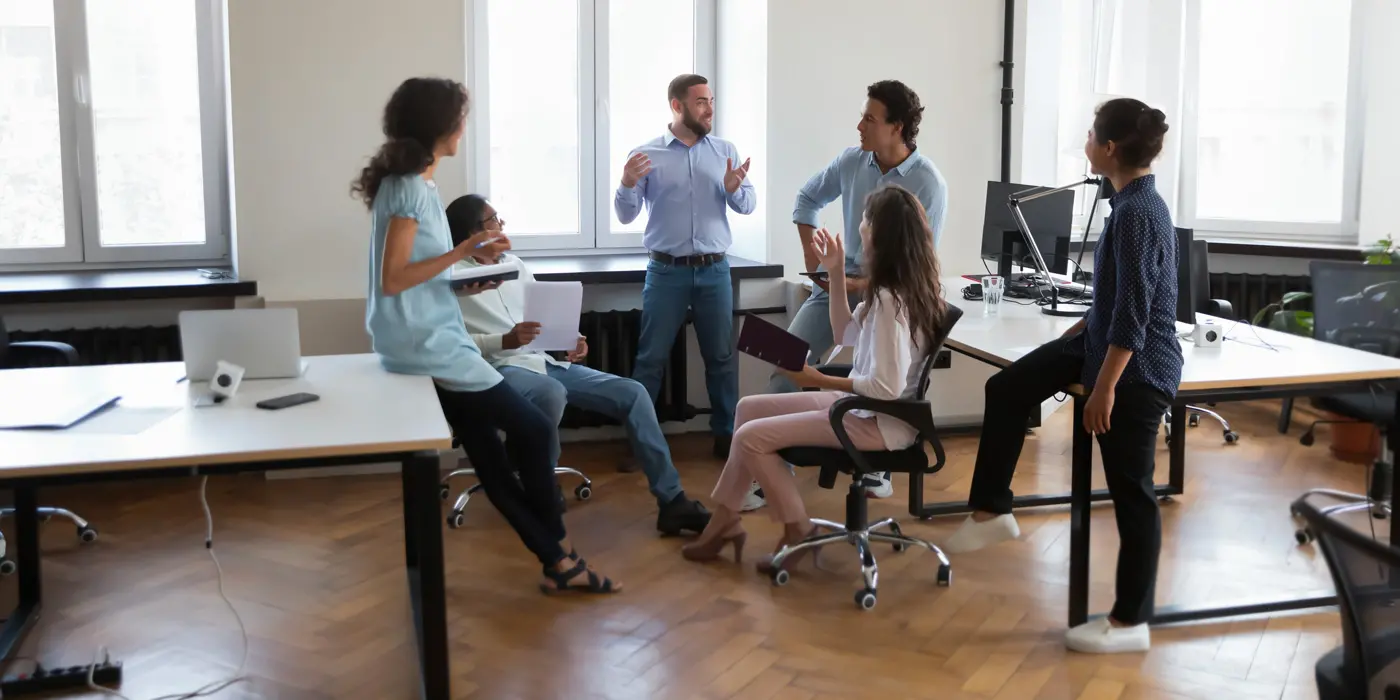 Quattro professionisti sorridenti riuniti attorno a un tavolo modulare in una luminosa sala riunioni a Torino all'interno del nostro Coworking.