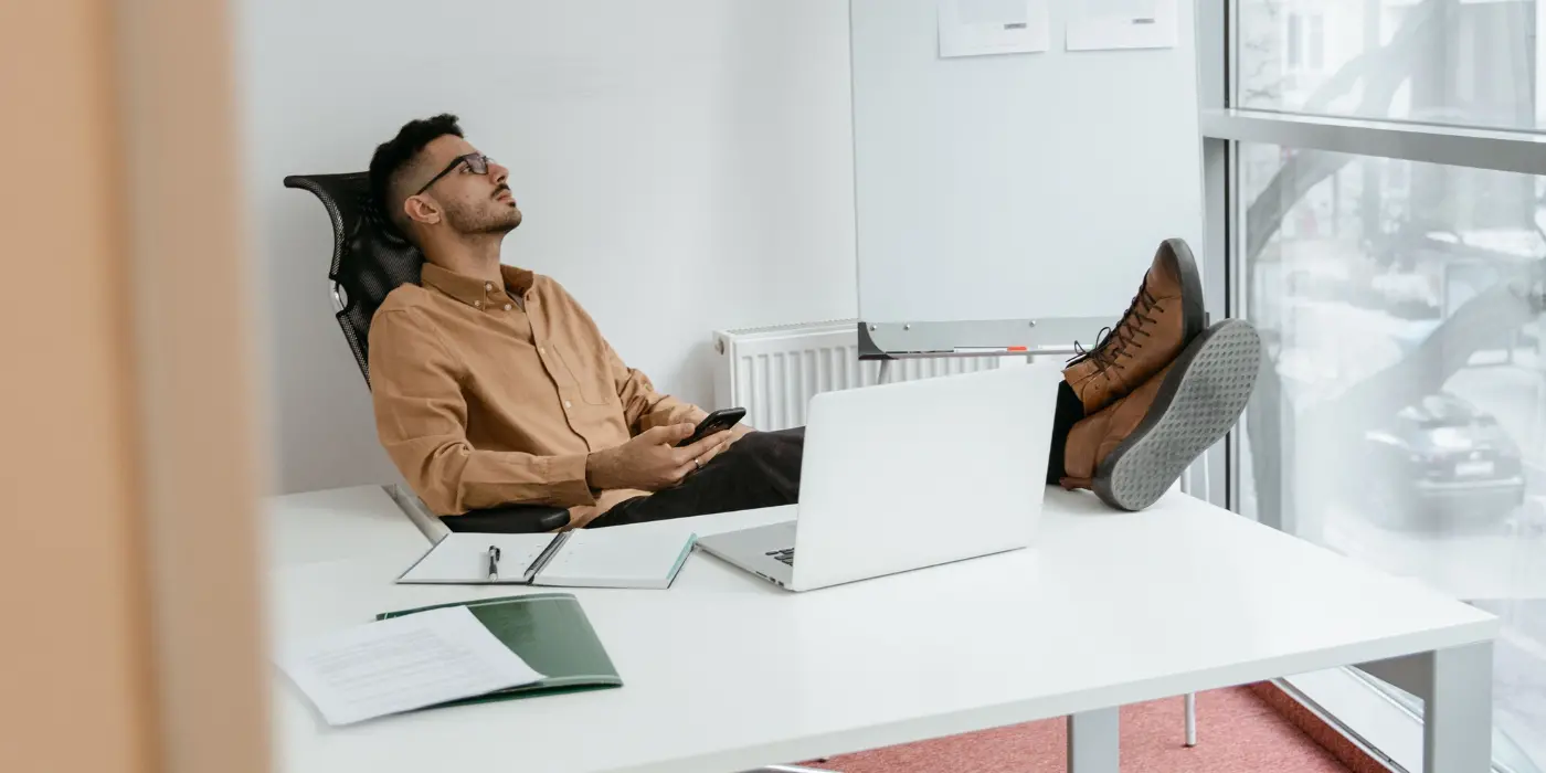 Professionista rilassato alla scrivania in un coworking ufficio silenzioso a Torino, mentre si gode un momento di pausa vicino alla finestra luminosa.