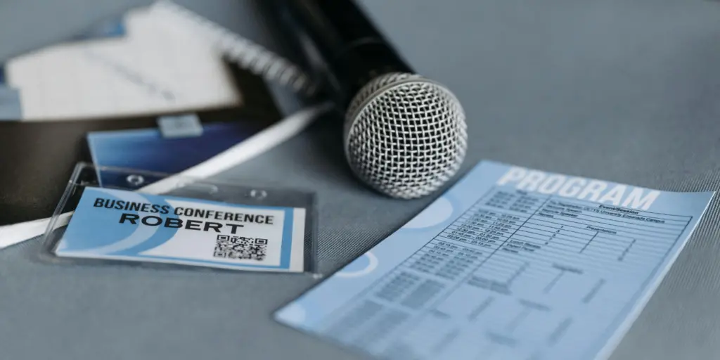 Dettaglio del materiale organizzativo sul tavolo per un evento aziendale, comprensivo di microfono wireless, badge per i partecipanti e programma dei lavori.